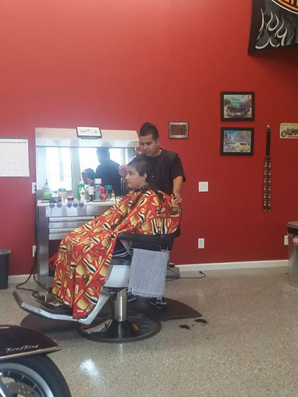 A barber cuts hair while a client sits in a salon chair draped in a colorful cape, surrounded by salon tools and decor.
