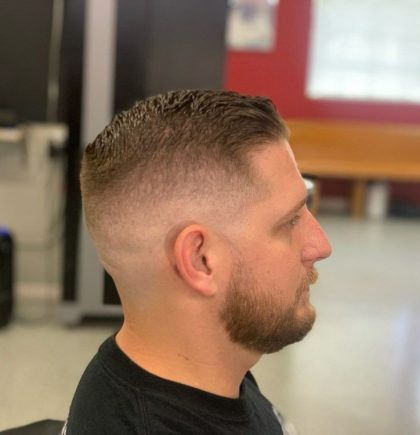 A person with a stylish short haircut, featuring a clean fade, seated in a barbershop with bright red walls in the background.