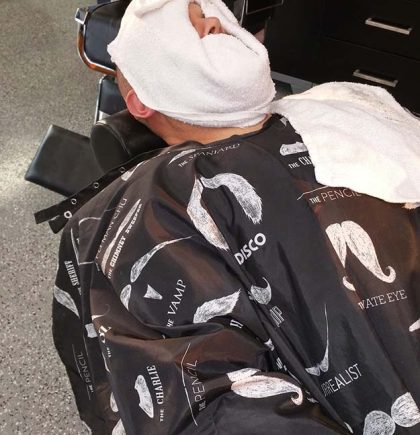 A toddler wearing a red shirt sits in a high chair, looking curiously at the surroundings.